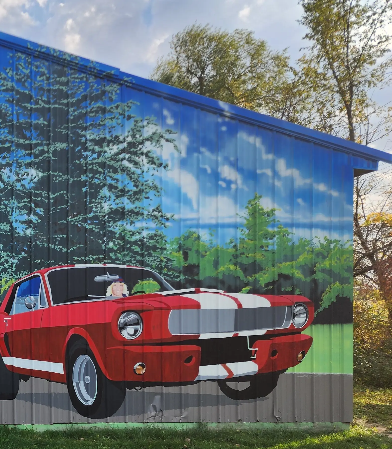 Mural of a red Mustang under tall pine trees on a building wall